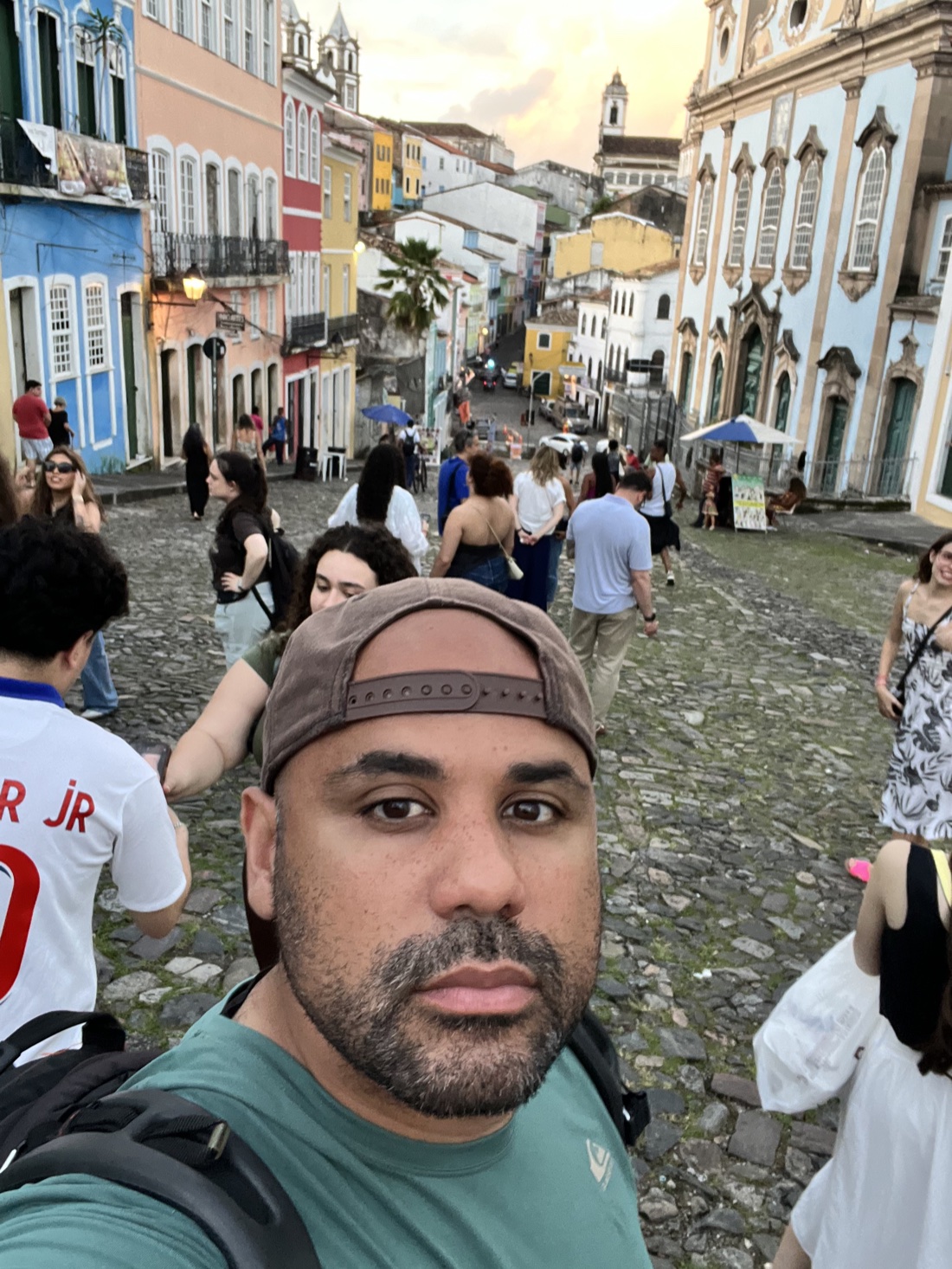 Jorge Gomez on location in Salvador, Brazil, backpack on his shoulder, on a cobblestone street lined with colourful colonial buildings